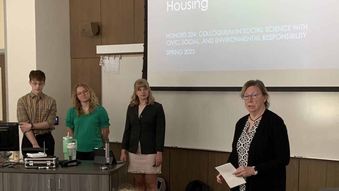 three students stand at the front of the room giving a presentation