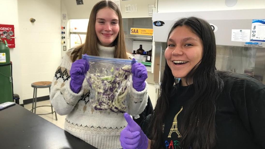 two students smile holding bag of kimchi