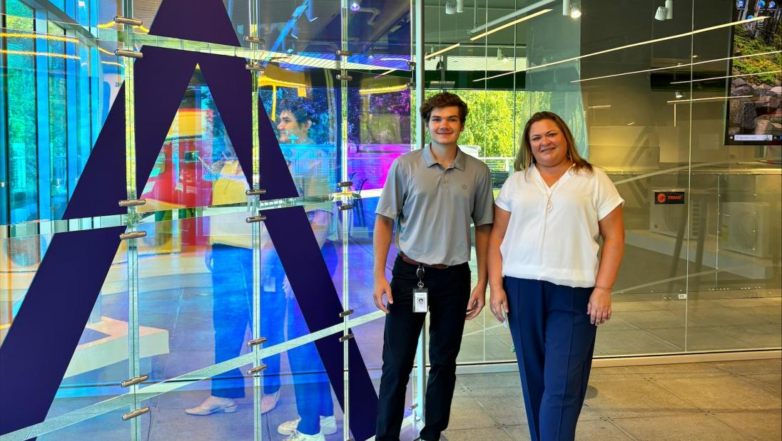 Marketing student, Evan Johnson, and his manager standing next to company logo at his internship at Trane.