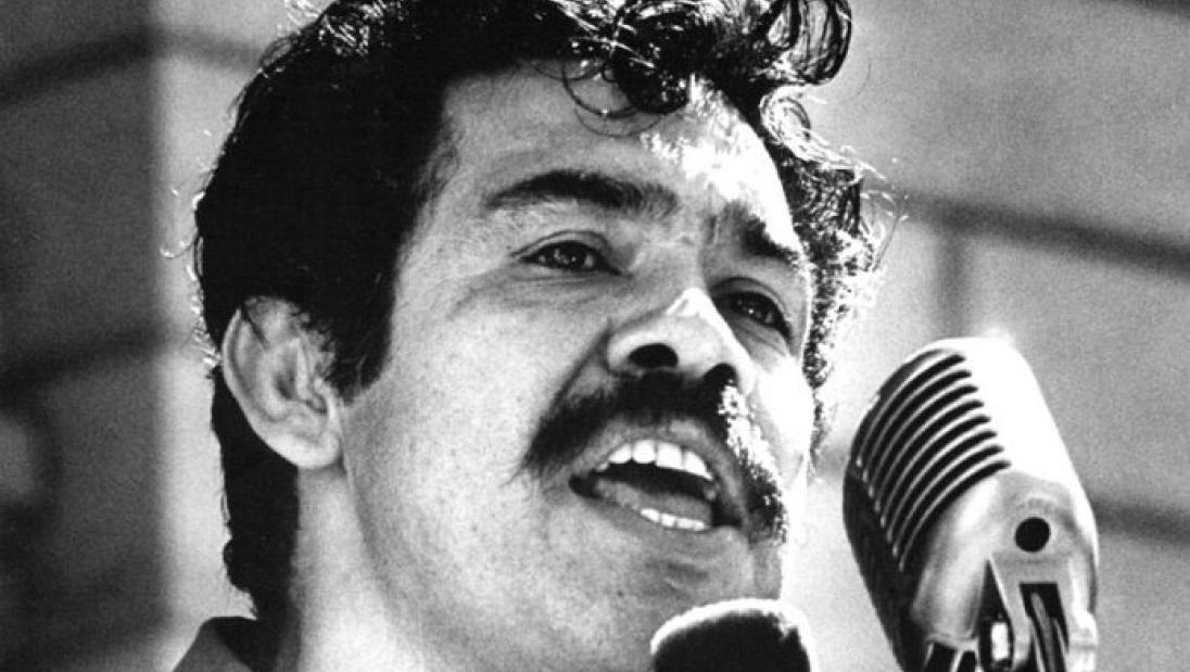 Black and white picture of a man speaking into a microphone at a lecturn.