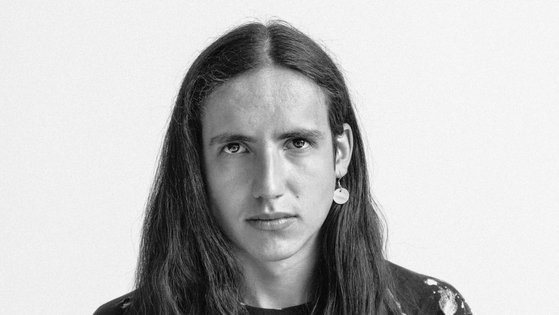 A black and white image of a person with long hair faces the camera.