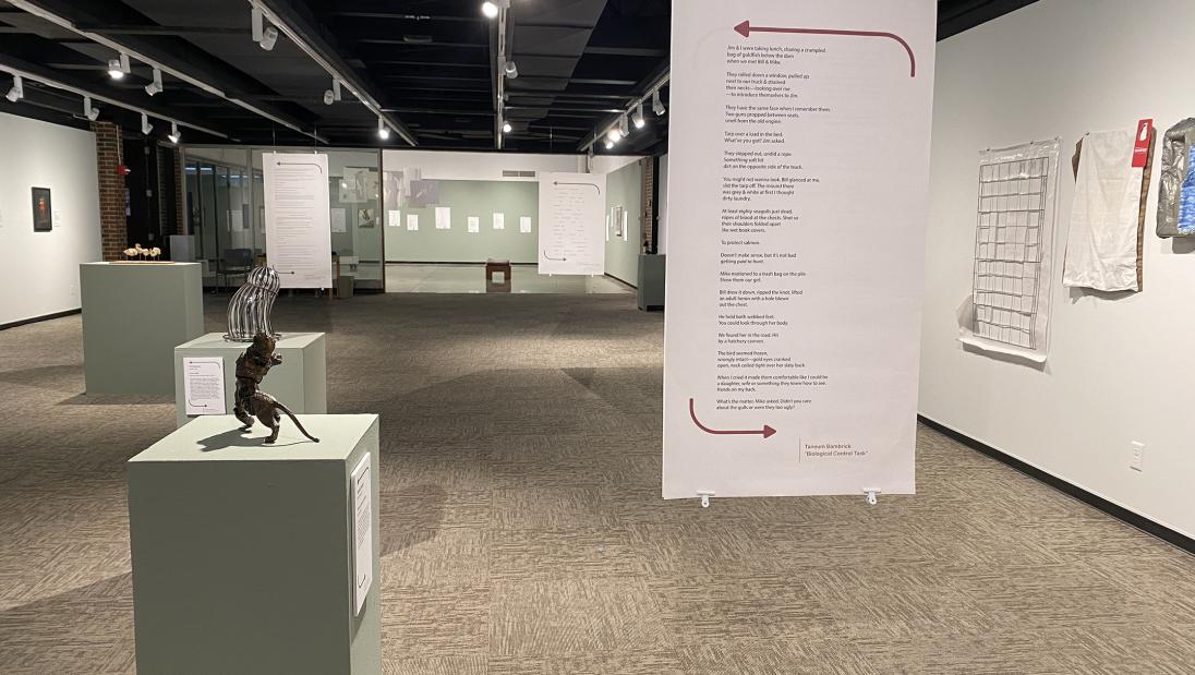 A poem printed on large paper hangs from the ceiling while artwork rests on pedestals in the background