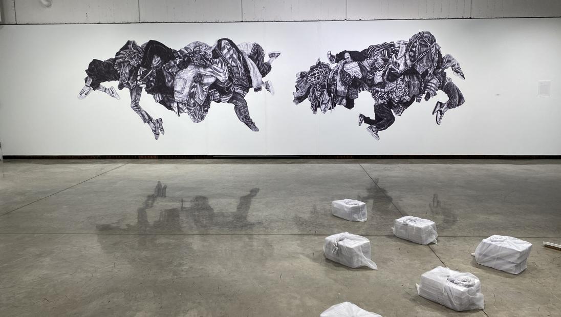 Sculpural installation lays on the floor in the gallery with a large mural wheat-pasted to the wall in the backgound
