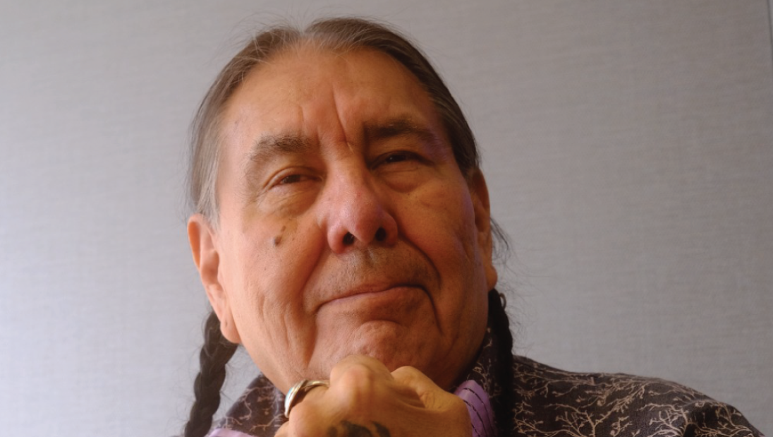 A man faces the camera with a tattooed fist in front of his mouth.