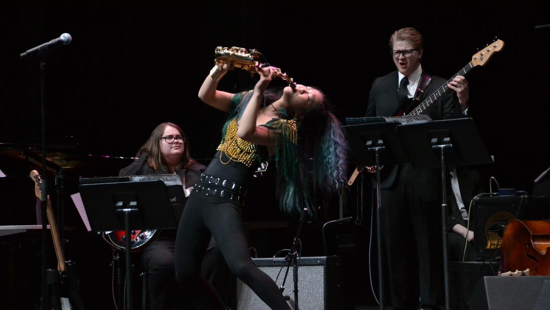 Student leans back while playing a saxophone on stage