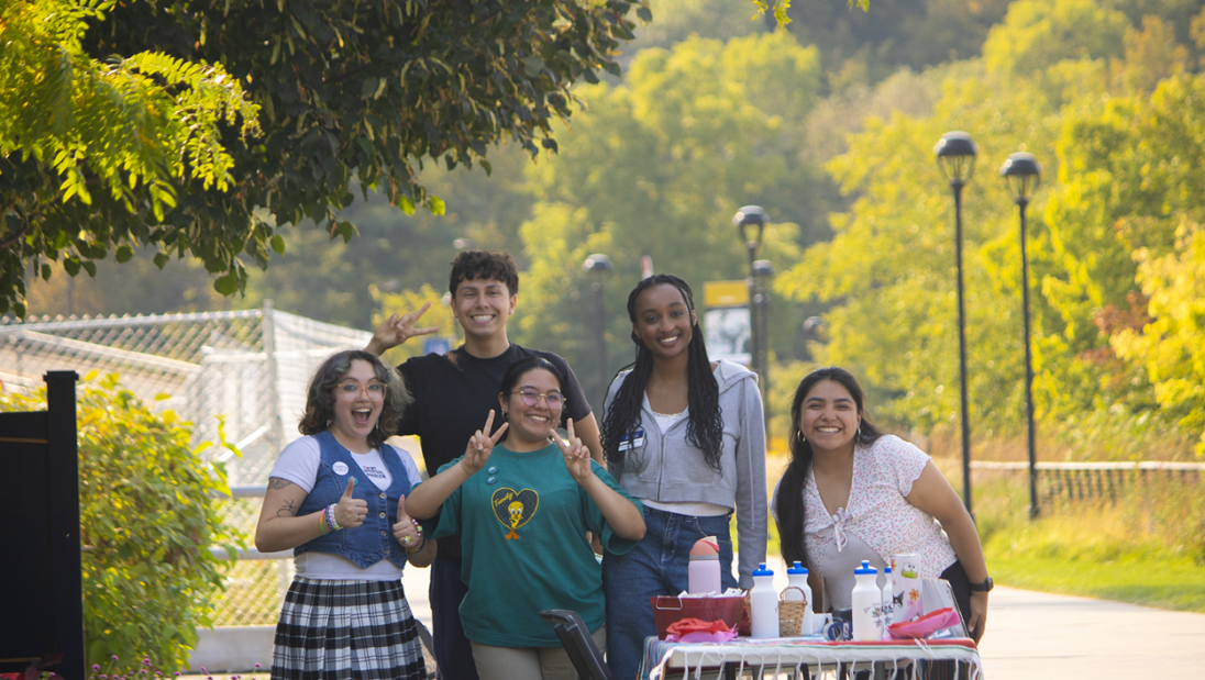 A small group of students standing behind a table smile and pose for a photo