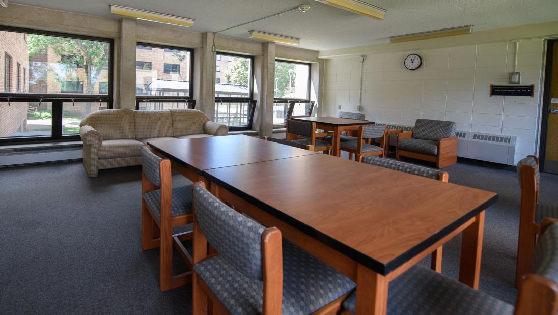 A common space in Sutherland Hall with multiple windows, a couch and many tables and chairs