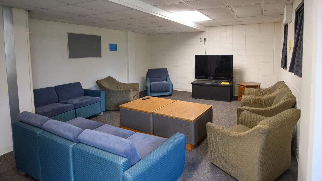A common area featuring two couches and multiple armchairs surrounding a television