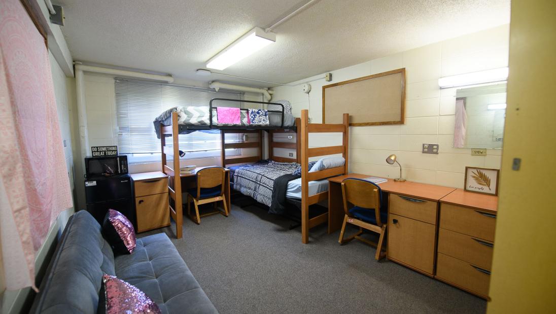 A room in Governors Hall with two bunked beds, two desks, a mini fridge and a couch.