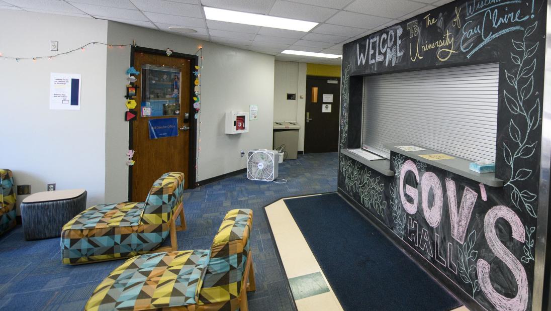 Lobby area of Governors Hall with colorful chairs and a welcome desk surrounded by a chalkboard wall decorated with a "Welcome to UWEC" message.