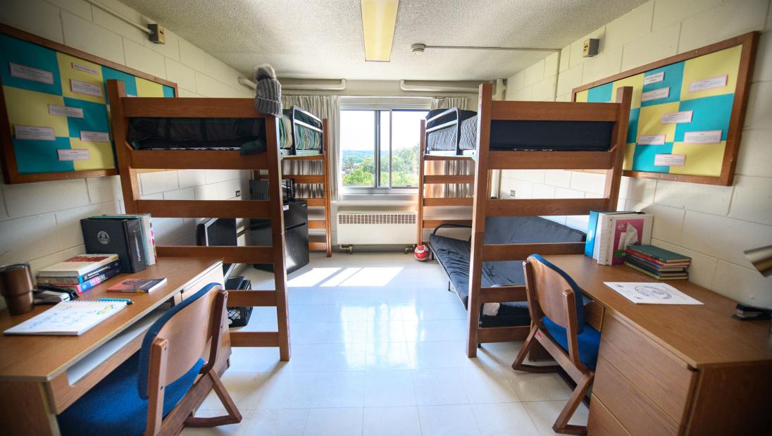 Horan Hall Room with two beds lofted bed, chairs, desks, and a big window. A futon is under one bed and a TV and mini fridge is under the other.