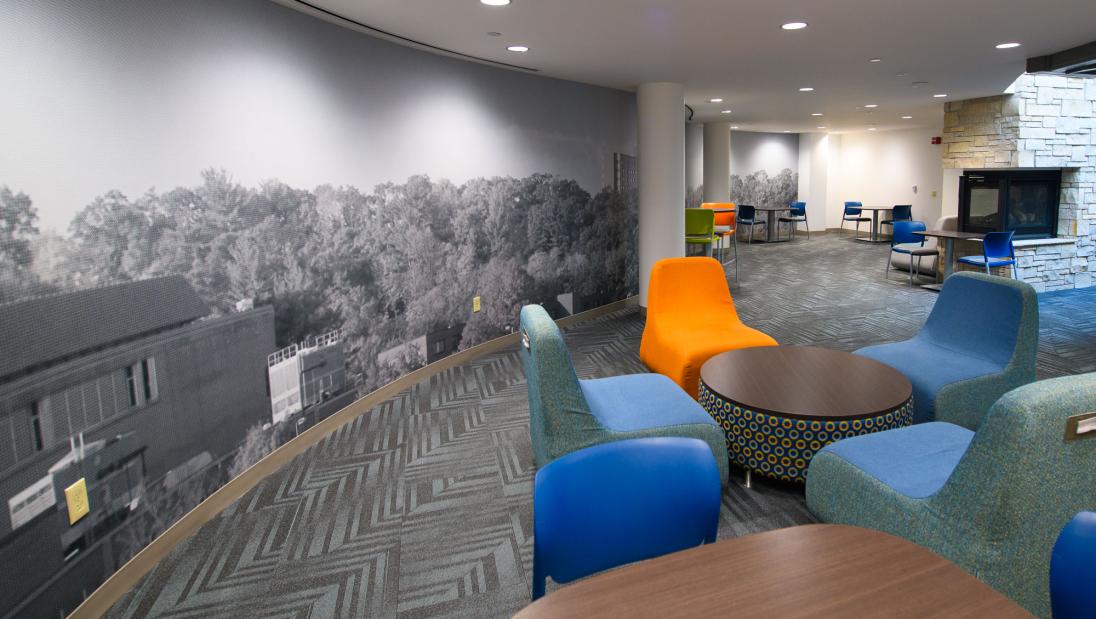 Common space in Towers Hall with colorful chairs, tables, and a big mural.
