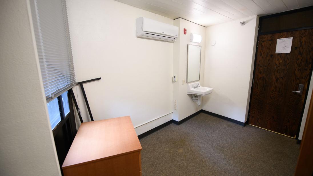 Alternate view of single room in residence hall with a sink, mirror and door to unit