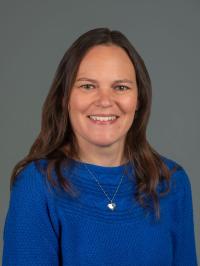 Picture of brown haired individual with blue sweater on a gray background