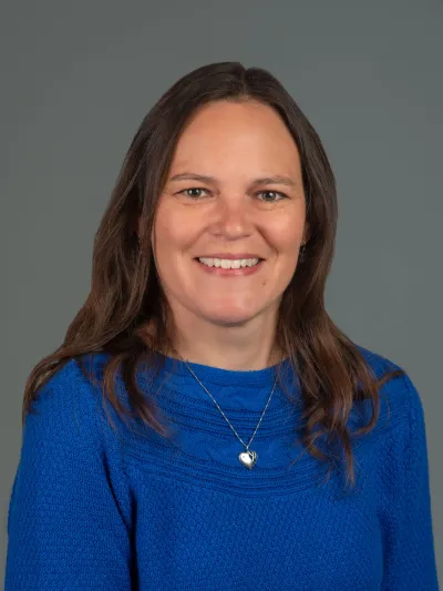 Picture of brown haired individual with blue sweater on a gray background