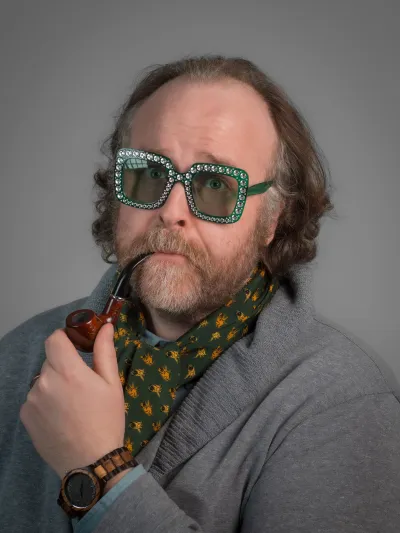 A very handsome gentlemen poses eloquently with a meerschaum pipe and rhinestone glasses on. He is a goofball.