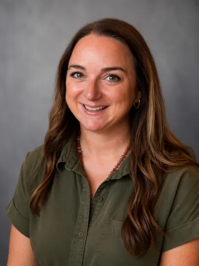 Headshot of Katelyn Leggio with long brown hair in a green short sleeved dress.