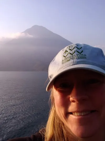 A person smiling in front of water and a mountain