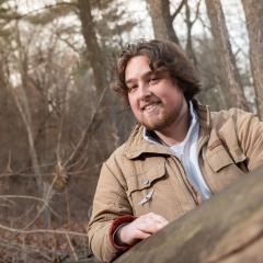 Ryan Pelle smiles at camera in a wooded background