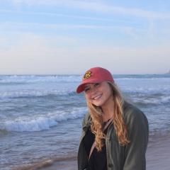 Blond female sitting on a hill with wide vista behind her, baseball cap