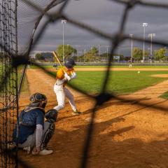 A view from behind the net showing a baseball batter preparing to hit a pitch during a game