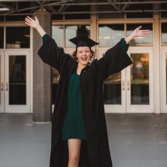 cap and gown wearing female graduate with arms up in the air