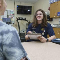 A student intern wearing a stethoscope and holding a clipboard, engaging in a discussion with another student
