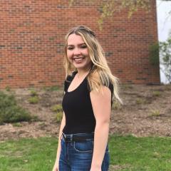 blond female student in front of Schneider Hall, smiling 
