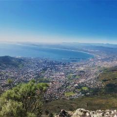 A view from Table Mountain in South Africa, overlooking Cape Town and its surrounding landscape, with the cityscape stretching towards the horizon and the ocean in the background.