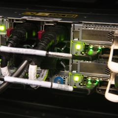 A close-up of the back of a supercomputer with multiple cables and connections illuminated by green indicator lights.
