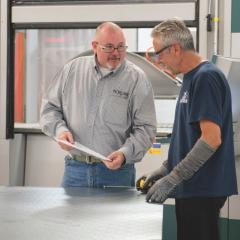 Two men collaborate over a document in an industrial space.