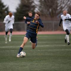 College student wearing a navy soccer uniform prepares to kick a soccer ball on a grass field.