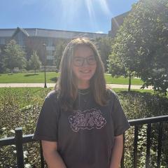 Katherine Manninen smiles at the camera against a sunny background of UWEC's campus.