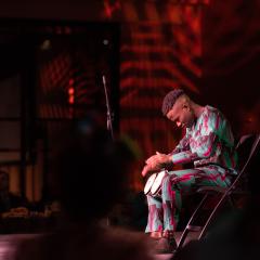 Olu Famule drumming on a stage in Nigerian traditional clothing