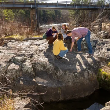 students and faculty on large river boulder for geology class 