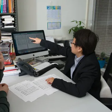 Two people look at a computer screen showing sheet music