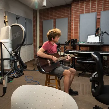 Student plays the guitar in UWEC's audio room 