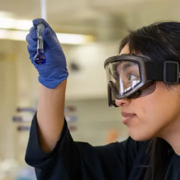 A student wearing safety goggles closely examines liquid in a small test tube