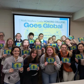 A group of students hold booklets in front of a computer display.