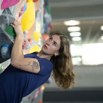 A student climbs a climbing wall looking determined.