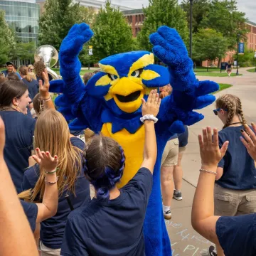 Blu celebrates the first day of school by putting their hands in the air alongside other students 