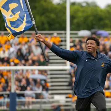 A blugold excitedly waves a UWEC flag during a football game.