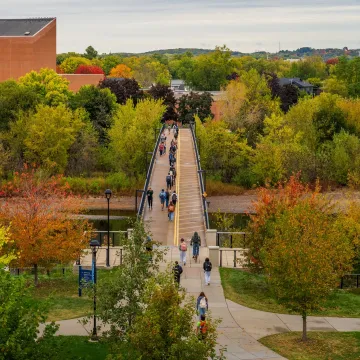 Students cross the bridge while fall colors surround them.