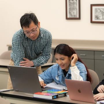 students and instructor in classroom at UWEC-BC, looking at a laptop and discussing 