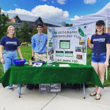 students in Geography club t-shirts at a table event outdoors