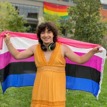 A person holding a pride flag smiles for the camera. 