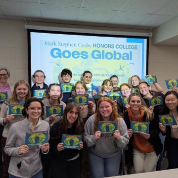 A group of students hold booklets in front of a computer display.