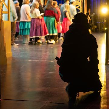 stage hand kneeling on right side of stage, cast onstage in costumes 
