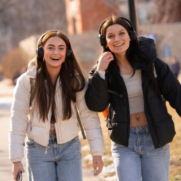 Two students walk across campus smiling at the camera.