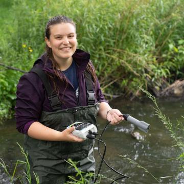 student in waders using instruments to measure creek water